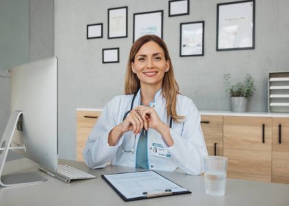 istockphoto-1424397493-612×612 Portrait of female doctor sitting behind desk in office and working on computer.