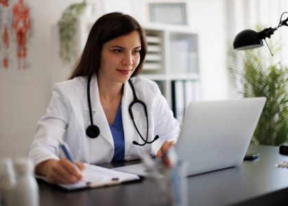 Smiling female doctor taking notes while working on laptop in the office Smiling female doctor taking notes while working on laptop in the office